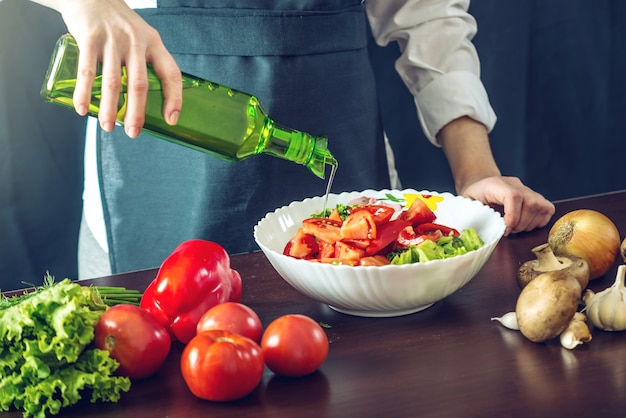 Chef in grembiule nero che prepara un'insalata di verdure