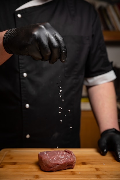 Chef in black gloves marinates steak in the kitchen