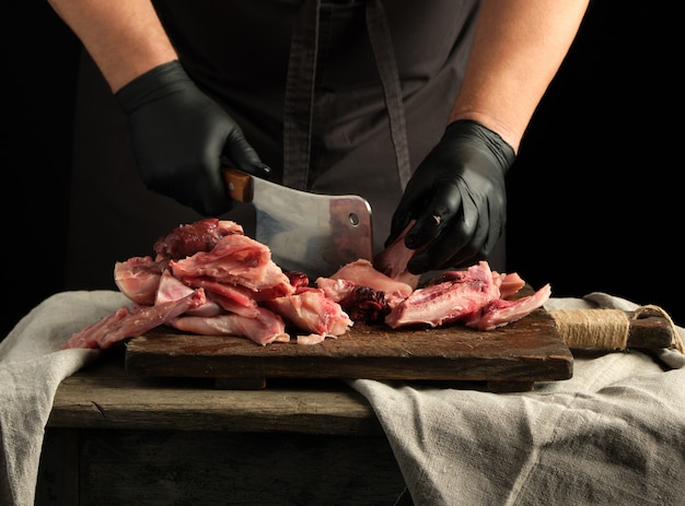 Chef in black latex gloves holds a big knife and cuts into pieces raw rabbit meat