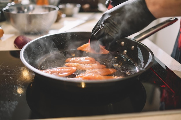 검은 고무 장갑을 낀 요리사는 냄비에 토마토를 튀긴다