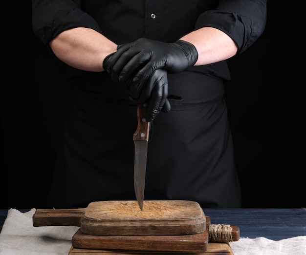 Chef in a black shirt and black latex gloves holds a vintage kitchen knife for cutting meat