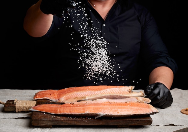 Chef in a black shirt and black latex gloves prepares salmon fillet