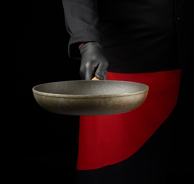 Шеф-повар в черной униформе и черных латексных перчатках держит пустую круглую сковороду