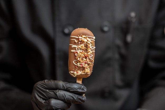 Chef in black uniform holding chocolate ice cream on a stick closeup