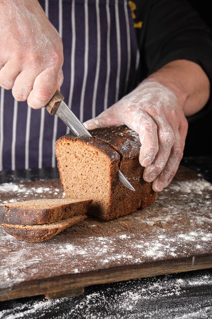 Chef in black uniform holds a kitchen knife in his hand and cuts off pieces of bread 