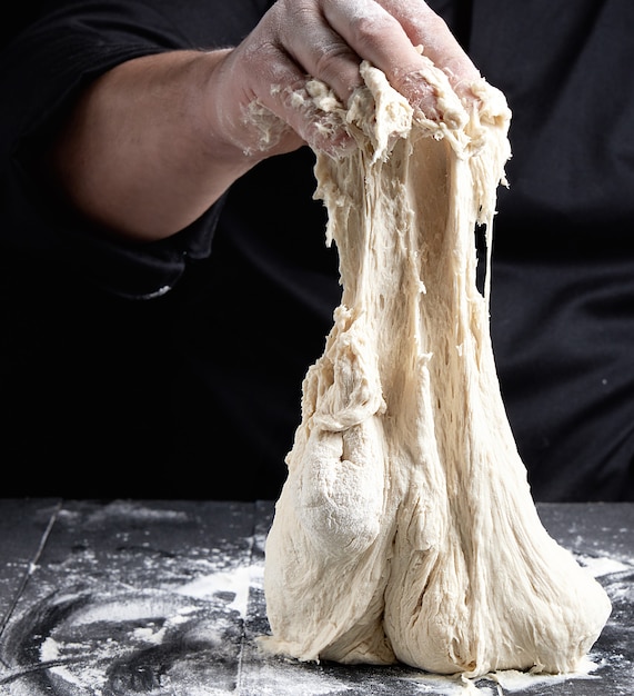 Lo chef in uniforme nera impasta l'impasto bianco di farina di frumento