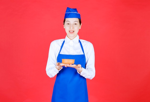 Chef in blue apron holding a pottery bowl. 