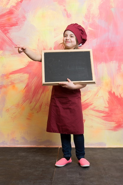 Foto bambino chef in grembiule su sfondo colorato piccola ragazza o sorridente cuoco con cappello con lavagna cucina e istruzione ristorante e menu design spazio copia felicità e infanzia