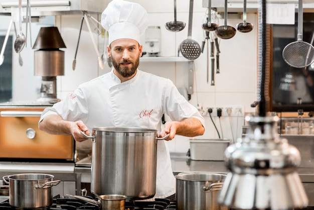 Фото Шеф-повар в униформе готовит суп в большой плите на кухне ресторана