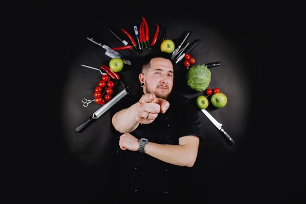 Chef cook lies between vegetables on a black background. Top view.