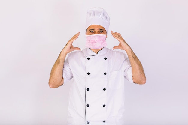 Шеф-повар в кухонной куртке и шляпе, надевая розовую маску, на белом фоне