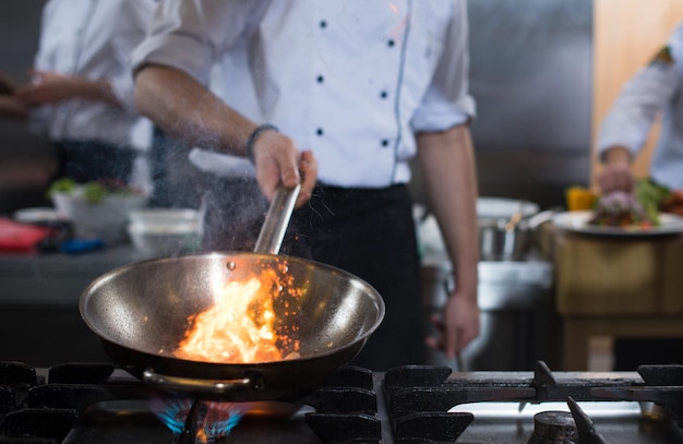 Photo chef cooking and doing flambe on food in restaurant kitchen