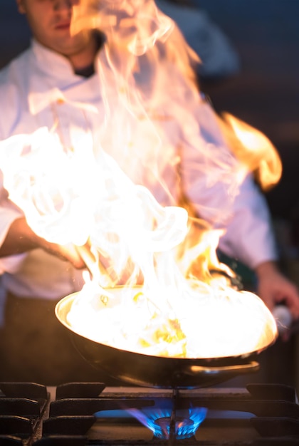Foto chef che cucina e fa flambe sul cibo nella cucina del ristorante