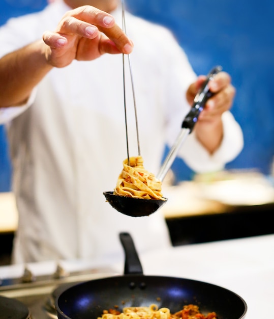 シェフがパスタを調理し、シェフが台所のプレートでスパゲティカルボナーラを提供
