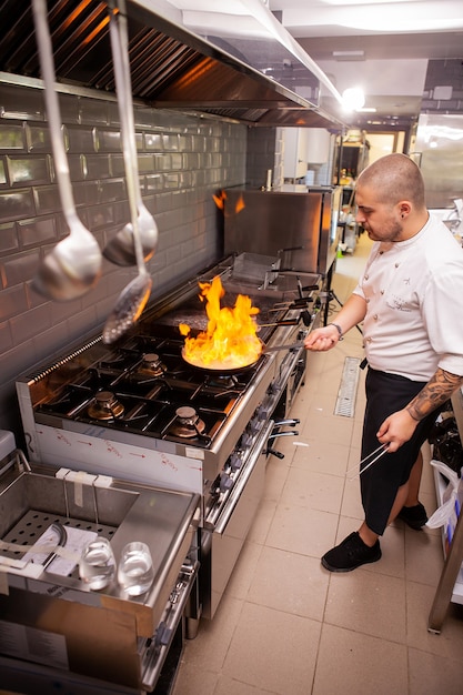 Foto chef di cucina con la fiamma in una padella su un fornello da cucina. in cucina ristorante