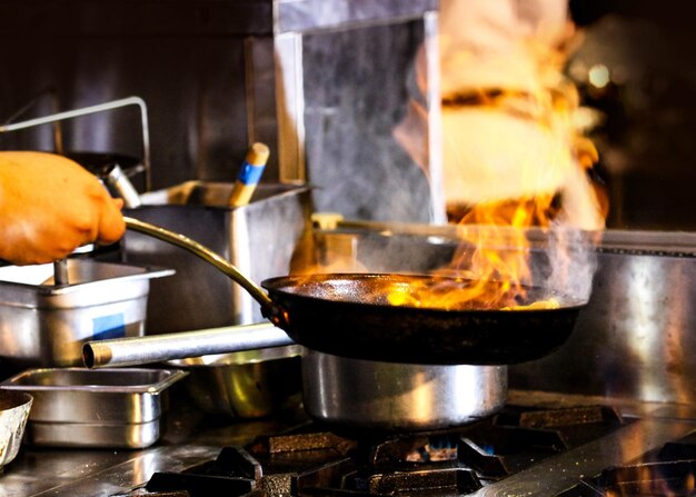 주방 스토브 에 있는 프라이팬 에 불 을 붙여 요리 하는 요리사