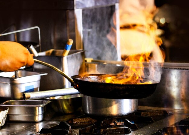 Chef cooking with flame in a frying pan on a kitchen stove