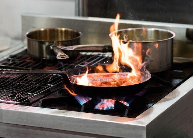 Chef cooking with flame in a frying pan on a kitchen stove