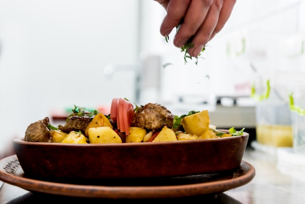 Chef cooks fried potatoes with pieces of meat in a restaurant kitchen