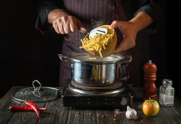 The chef cooks soup with pasta and vegetables in a saucepan