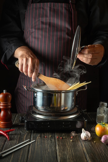 The chef cooks soup with pasta and vegetables in a saucepan