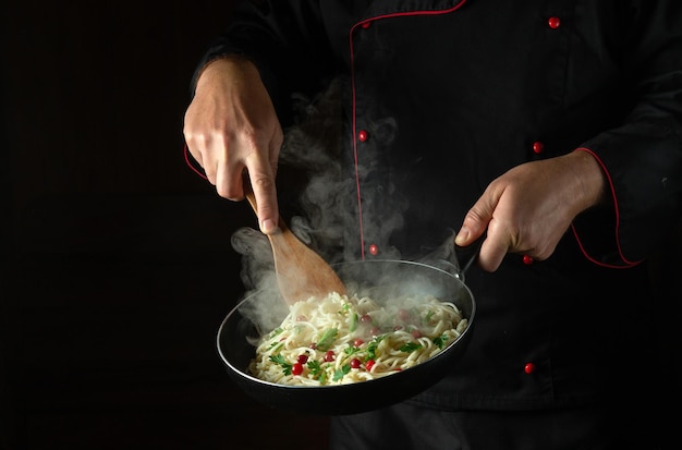 The chef cooks spaghetti in a hot pan Space for advertising on a black background Italian national cuisine