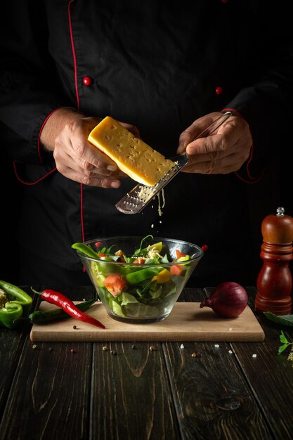 The chef cooks vegetarian food from fresh vegetables Menu concept for hotel on dark background Adding cheese to a salad