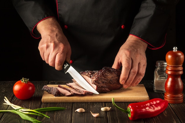 The chef cuts the baked beef meat on a cutting board