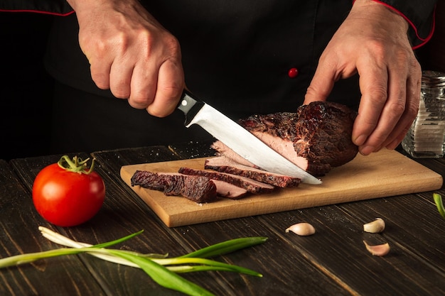 Chef cuts the baked beef steak with a knife on a wooden table