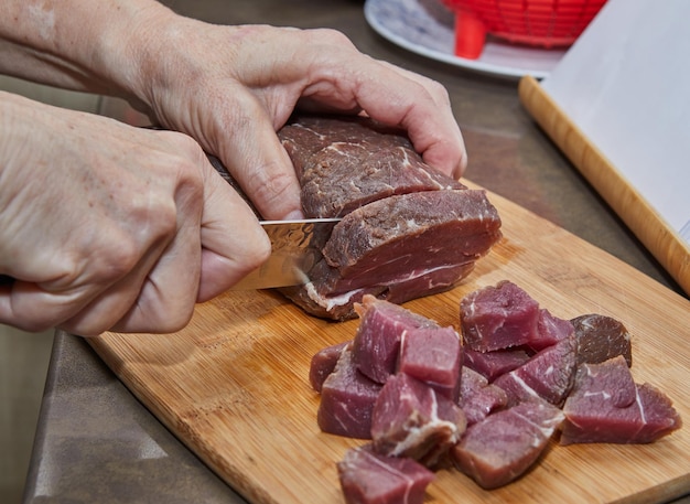 요리사는 쇠고기 고기를 요리를 위해 입방체로 자릅니다.