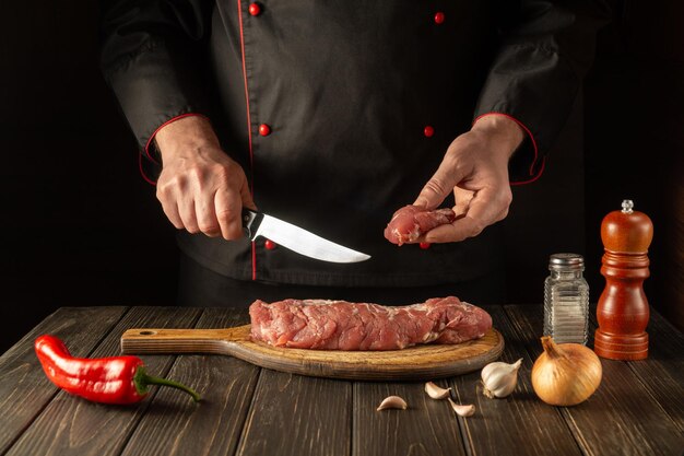 The chef cuts beef raw meat on a cutting board before barbecue