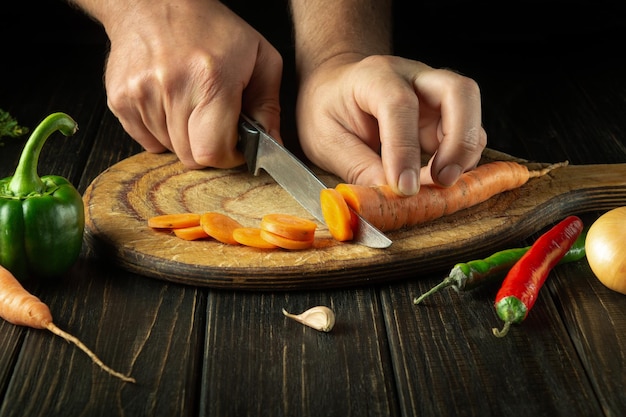 The chef cuts carrots into small pieces on a cutting board for preparing a vegetarian lunch or dinner Set of vegetables on the kitchen table