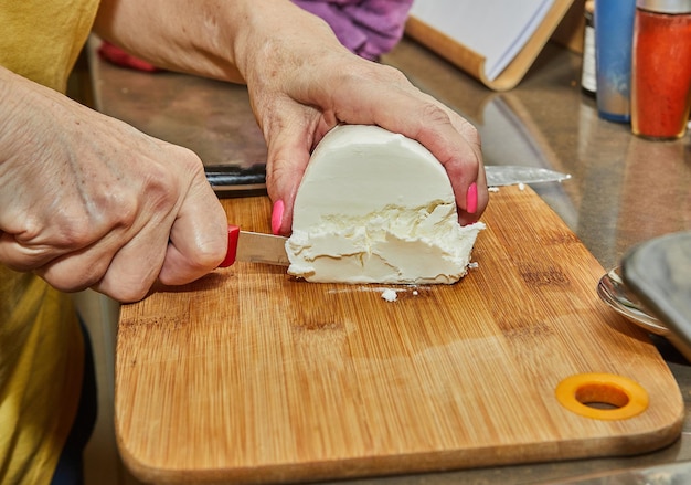 Chef cuts the cheese with knife on wooden board for making a pie