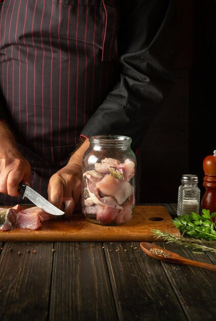 シェフはアロマティックなスパイスでキッチンテーブルの作業環境にヘリングを準備する前に魚をステーキに切ります