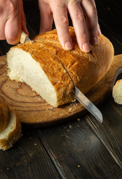 The chef cuts fresh bread with a knife on a kitchen cutting board for lunch