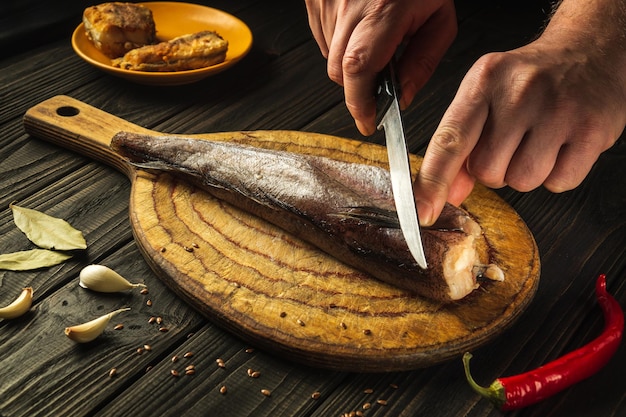 Lo chef taglia il pesce merluccius fresco su un tagliere di legno con un coltello