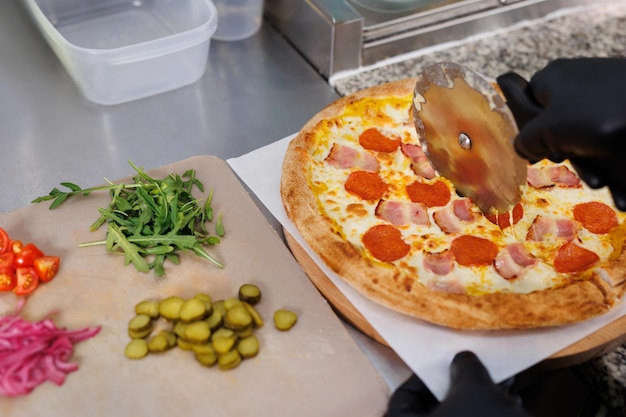 Foto il cuoco taglia fette di pizza appena preparate in cucina