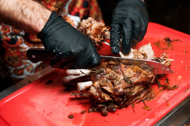 Шеф-повар режет сочное приготовленное мясо, отделяя мясо от кости ножом.
