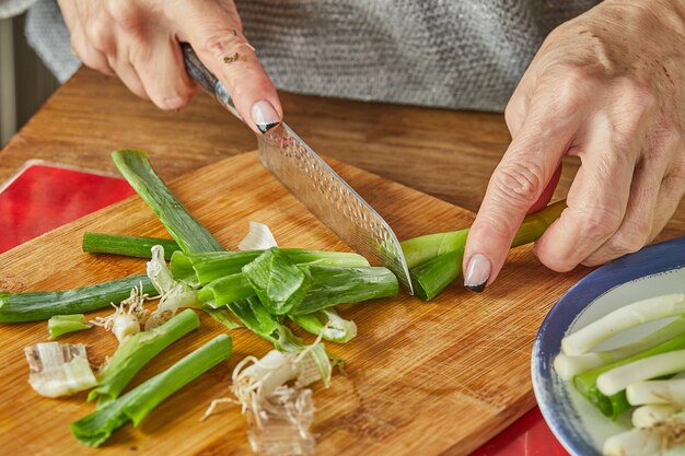 Chef cuts the leek in circles in the kitchen on wooden board