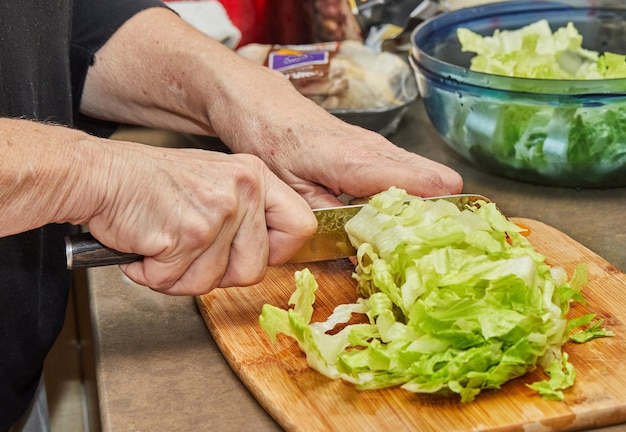 Chef cuts lettuce on wooden board in the home kitchen