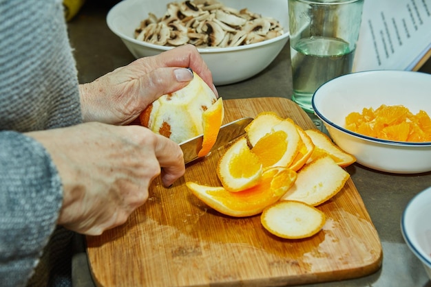 Photo chef cuts oranges to prepare salad with zucchini oranges and salami french gourmet cuisine on a wooden background