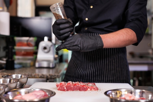 Foto lo chef taglia le costole di maiale, le sale e le peperone nella cucina del ristorante.