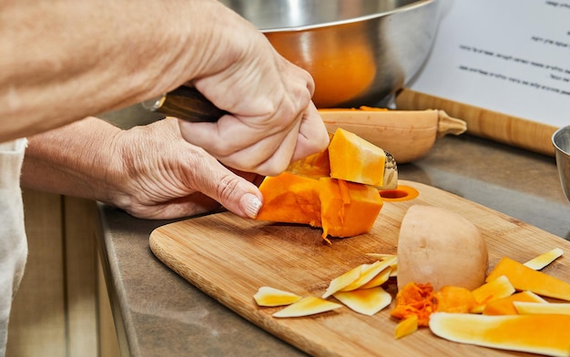 Chef cuts pumpkin in the shape of pear on wooden board in the home kitchen