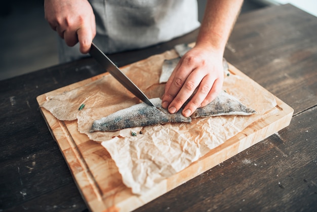 Photo chef cuts raw fish slices on wooden cutting board