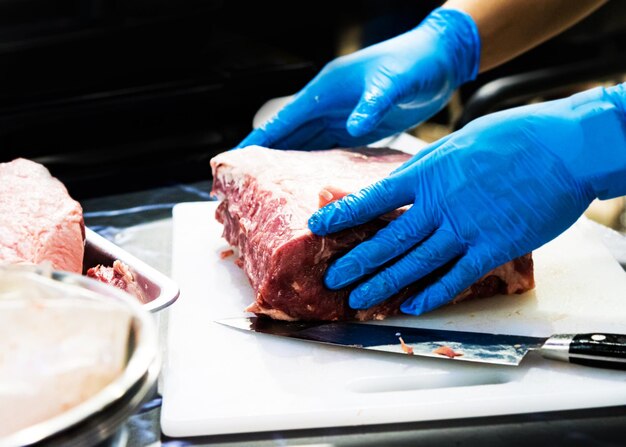 Photo chef cuts raw meat with a knife on a board cook cuts raw meat