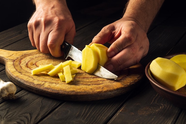 The chef cuts raw potatoes into small pieces with a knife