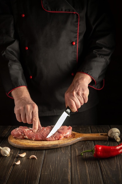 Photo chef cuts raw veal meat on a cutting board before baking cooking delicious food in the kitchen