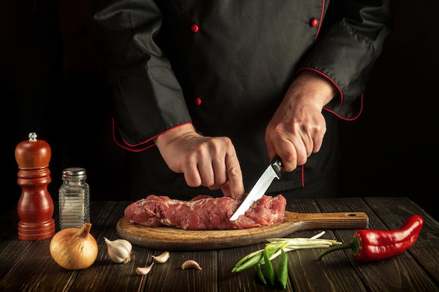 シェフは焼く前にまな板の上で子牛の生肉を切る キッチンで美味しい料理を作る