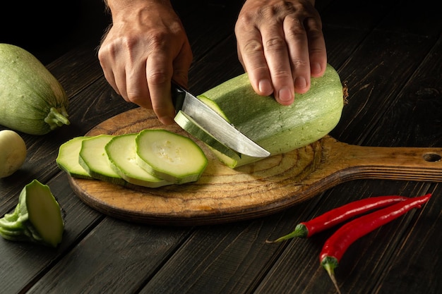 The chef cuts vegetable marrow into small pieces with a knife before preparing a delicious lunch