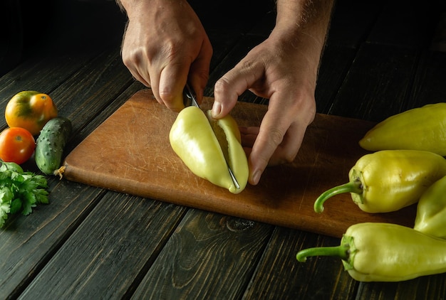 The chef cuts yellow fresh peppers on a cutting board to prepare a delicious lecho at home The idea of cooking a vegetable diet on the kitchen table